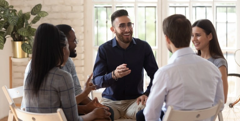 A group of people is sitting together in a comfortable living room, participating in a discussion with a support worker.