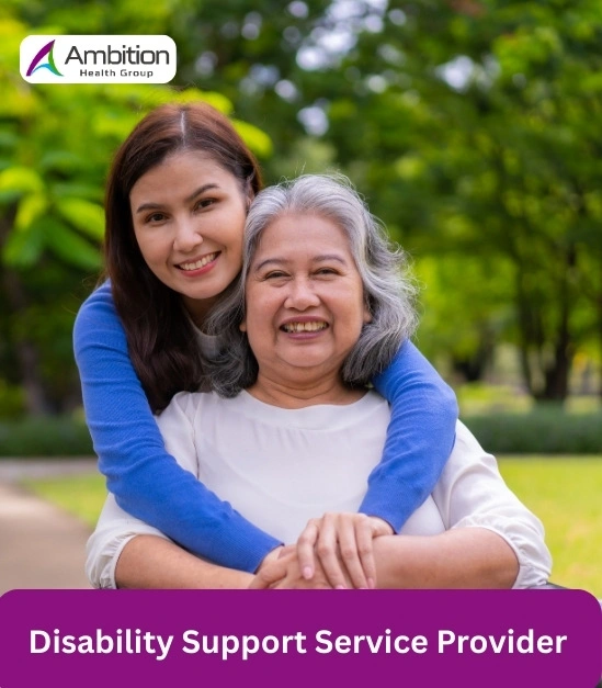 A caregiver in a blue shirt embracing an elderly woman in a white blouse with a smile.
