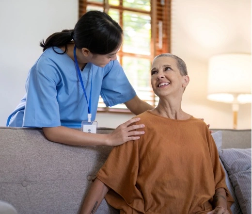 A caregiver in blue scrubs gently placing a hand on the shoulder of an elderly woman with a warm smile.