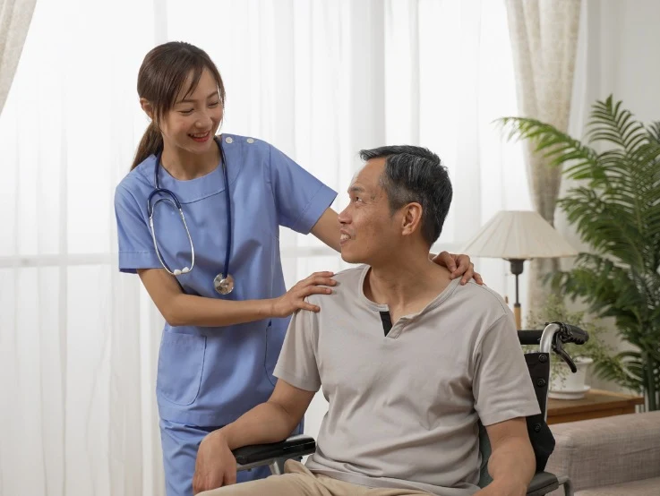 This image shows a healthcare worker in a light blue uniform, offering a comforting and supportive gesture to a man in a wheelchair